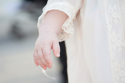 Mano de un bebé, cuelga sobre su faldón, se aprecia una piel muy blanca tomada por fotógrafos para bautizo en la Catedral de la Almudena.