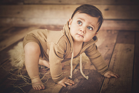 Foto de bebé de 12 meses, niño con ojos azules con body y capucha posando.