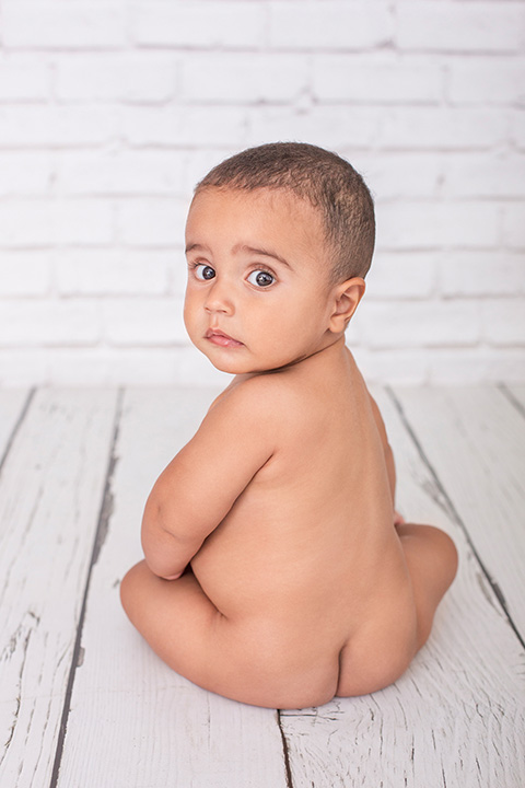 Foto de un niño de espaldas, sin ropa, posando para fotógrafos de bebés. 