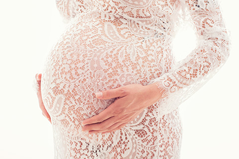 detalle de la barriga con las manos apoyadas y con un vestido de encaje blanco, muestra una fotografía de embarazada.