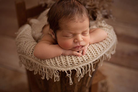 Bebé dentro de un cubo marrón dormido sobre una manta beige.