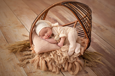 Niño bebé dormido sobre un soporte de circular con un oso pequeño en su mano.
