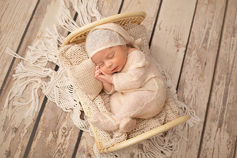 Precioso bebé dormido en una sesión de fotos de recién nacido, en una cama y vestido con un pijama beige.