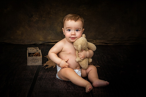 Niño en pañal abrazando oso de peluche y con una caja en su primera sesión de fotos de bebé.