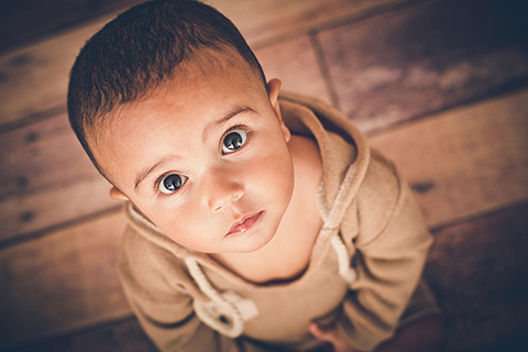 Niño en sesión de fotos de bebé de 12 meses, vestido en tonos tostados sobre suelo de madera.