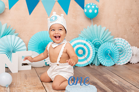 Fotografía de bebé en una sesión smash cake con una tarta y un decorado de cumpleaños en tonos azules y blancos.