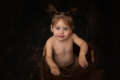 Fotografía de bebé en un cubo, niña con coletas sobre fondo oscuro en un estudio de fotografía de bebés en Madrid.