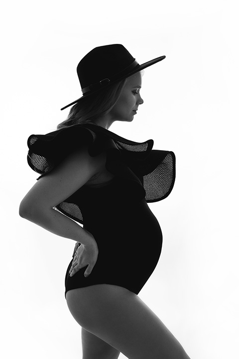 Mujer a contraluz con un sombrero y body negro, esta de lado mostrando su silueta y su barriga de embarazada.