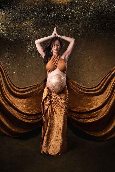 Mujer en una sesión de fotos de belly painting con técnica de pan de oro, tiene una espiral en la barriga, viste un top y una falda en color dorado.