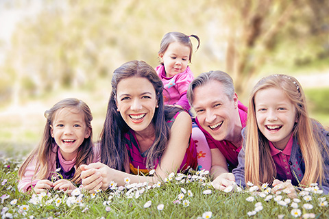 Familia de padres y tres hijas en una sesión familiar en exterior, están tumbados boca abajo mirando hacía la cámara, llevan ropa en tonos rosas.