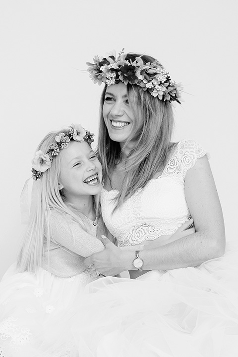 Madre e hija en una sesión con un fotógrafo de familia en Madrid, la imagen está tomada en blanco y negro, ellas se abrazan y ríen, ambas llevan corona de flores en la cabeza y visten vestido blanco.