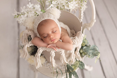 Precioso recién nacido dormido sobre un cubo blanco y rodeado de plantas y flores.