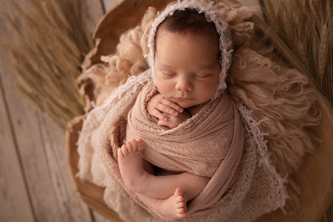 Bebé en estudio fotográfico, envuelto en una tela y dormido boca arriba dejando entrever sus manos y sus piernas.