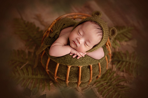 Bebé chino duerme en una cesta de bambú, rodeado de hojas verdes.